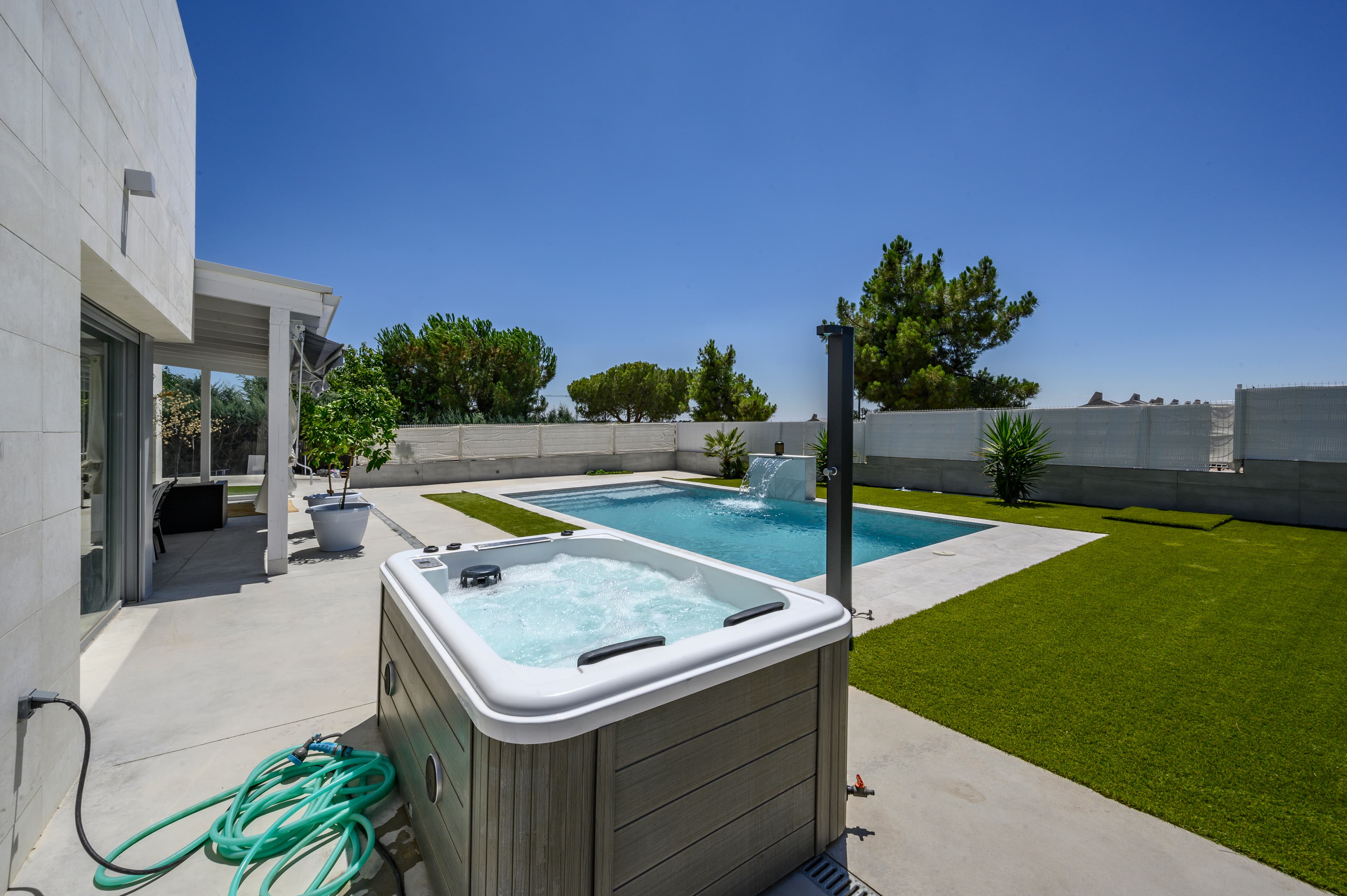 Jacuzzi exterior y piscina rectangular con surtidor en jardín privado