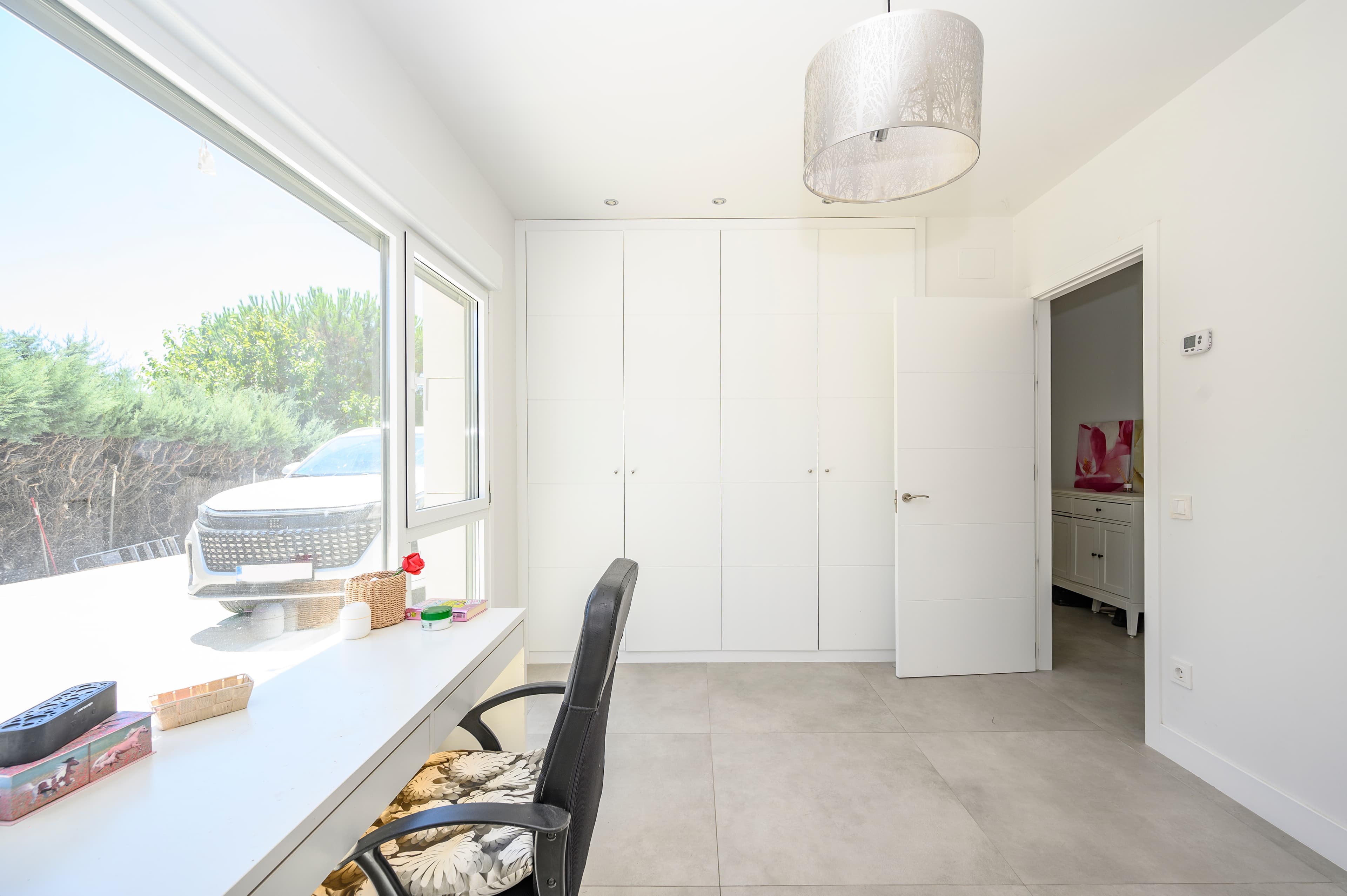 Habitación con escritorio empotrado bajo ventanal, armario blanco y suelo de gres gris