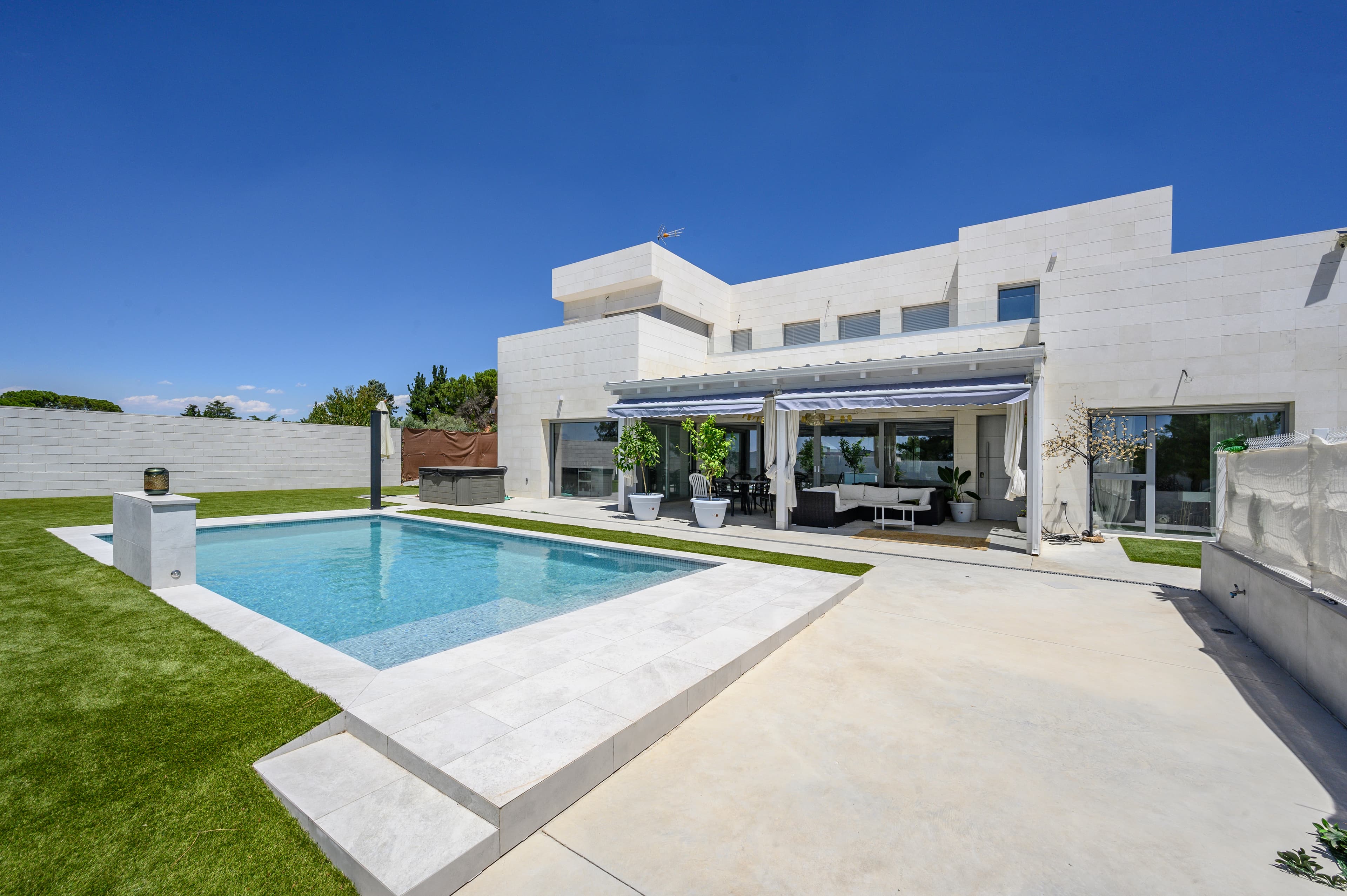 Vista trasera del chalet con piscina, terraza cubierta y toldos extensibles
