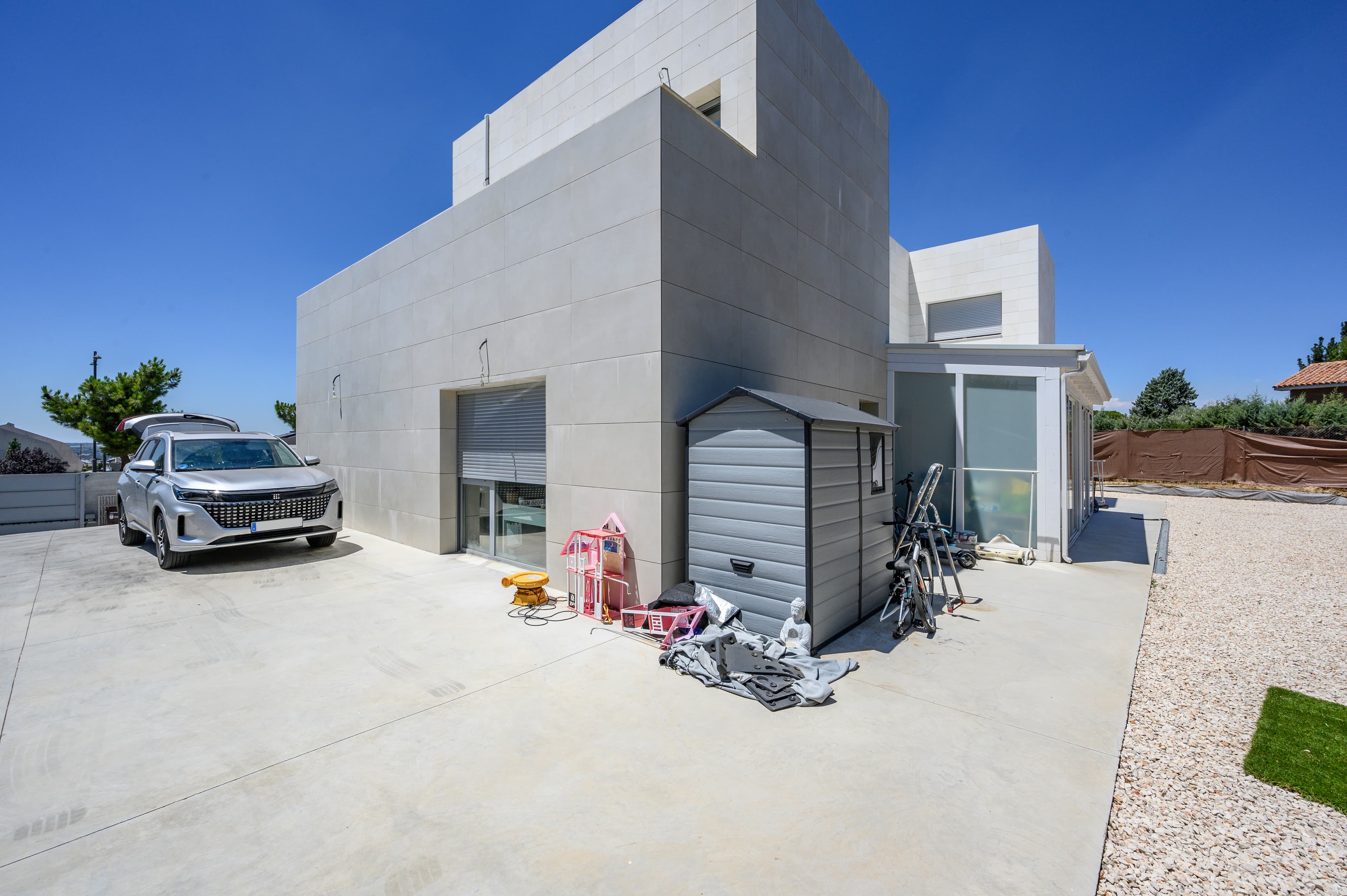 Lateral del chalet con zona de aparcamiento en hormigón y garaje con persiana