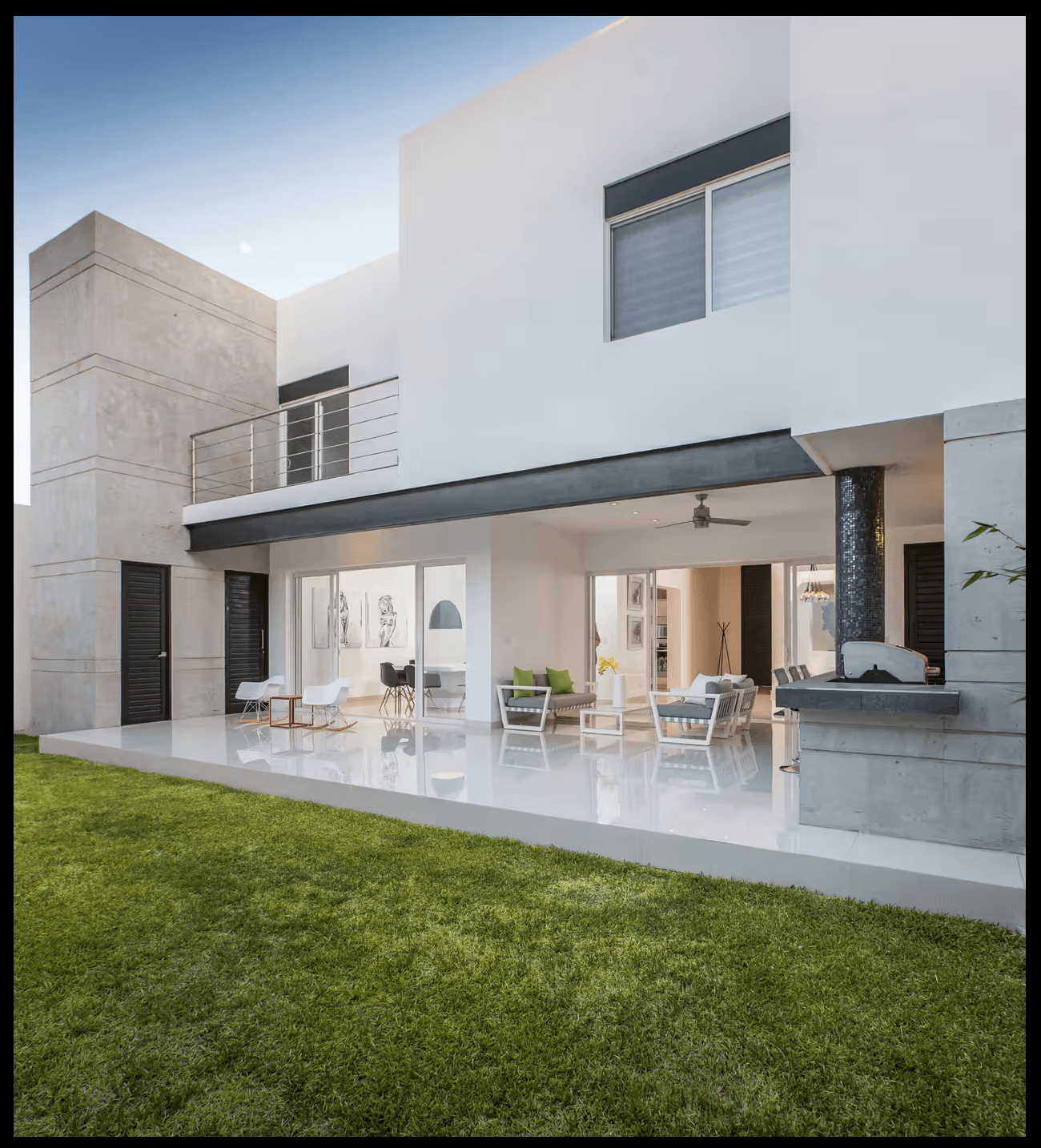 Fachada trasera con porche cubierto, terraza pulida y jardín de césped